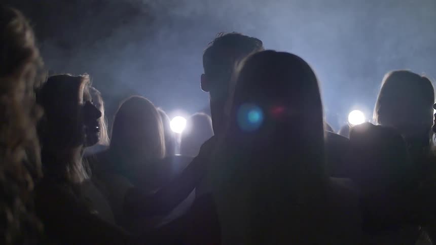 A crowd of women seductively caress a man in dark, foggy room with one bright light