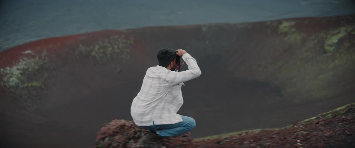 Photographer crouches on rim of volcano crater taking and takes a photograph