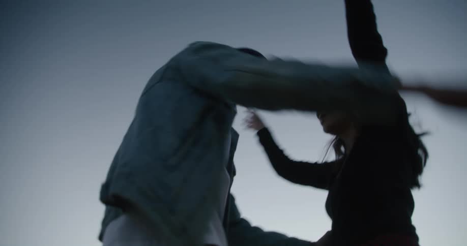 Young couple dancing and hugging in front of a parked vehicle on a field at evening