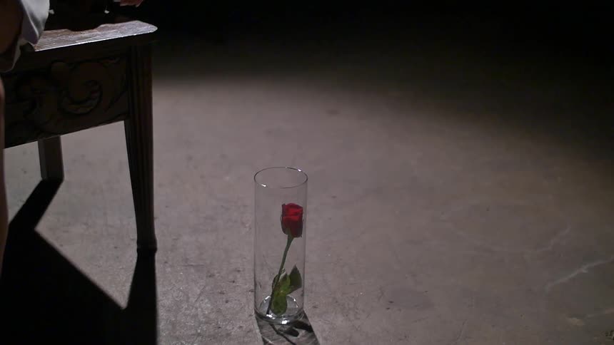 A glass sits on the floor with a rose in it