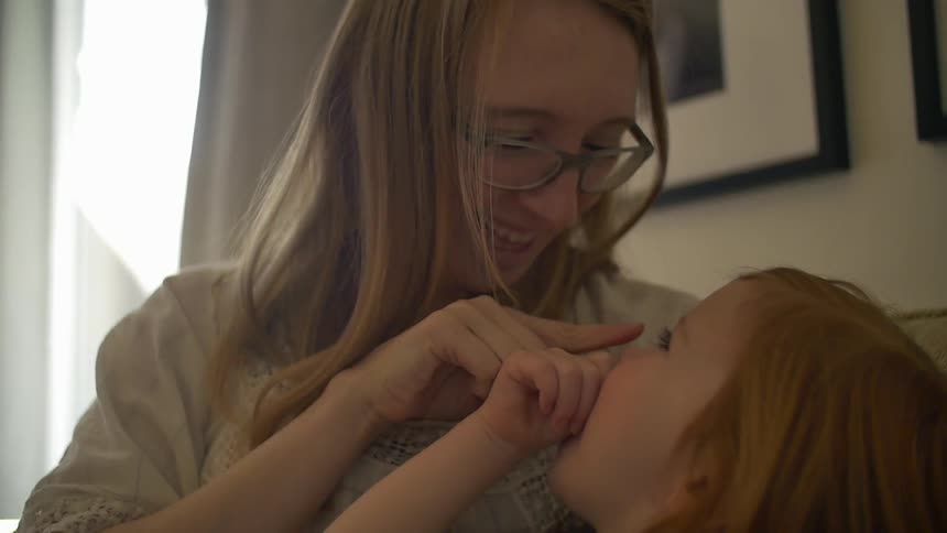 A woman smiles grabs her child's nose and gives her a kiss