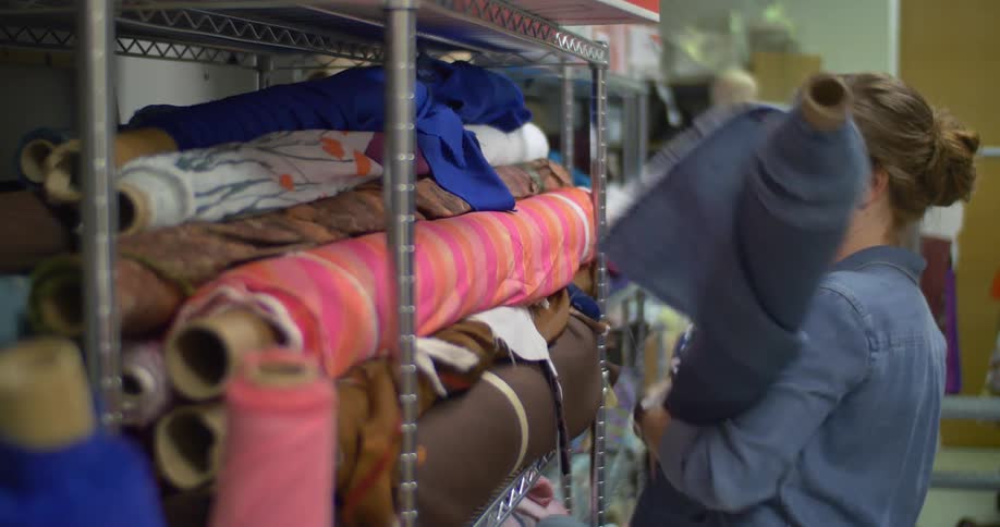 A woman pulls rolls of fabric from a rack