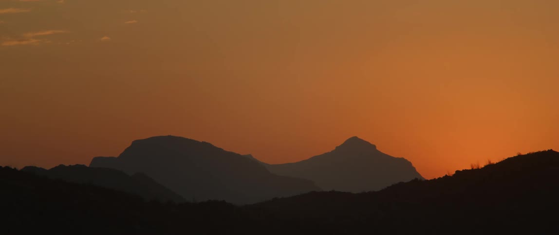 The sky turns orange as the sun sets over a mountain range