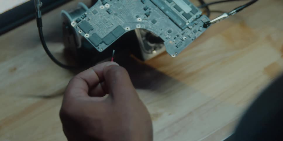 A man is sitting at a table working on an electronic component and he cuts the plastic from the ends of a piece of wire