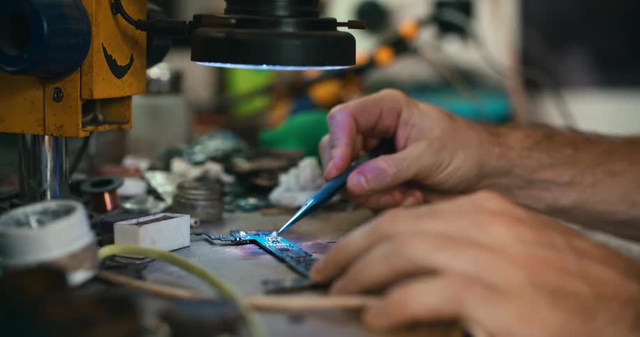 A man is sitting at a work station soldering an electronic component
