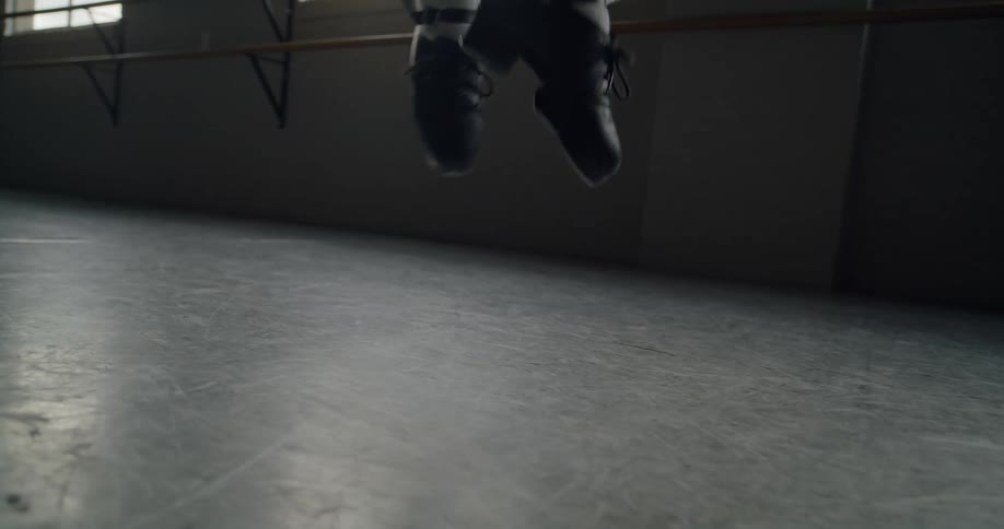 A ballet dancer wearing heeled shoes does a plie jump in a dance studio