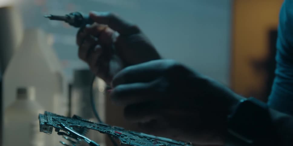 Smoke rises from a soldering iron as a man uses it to attach a wire to a circuit board