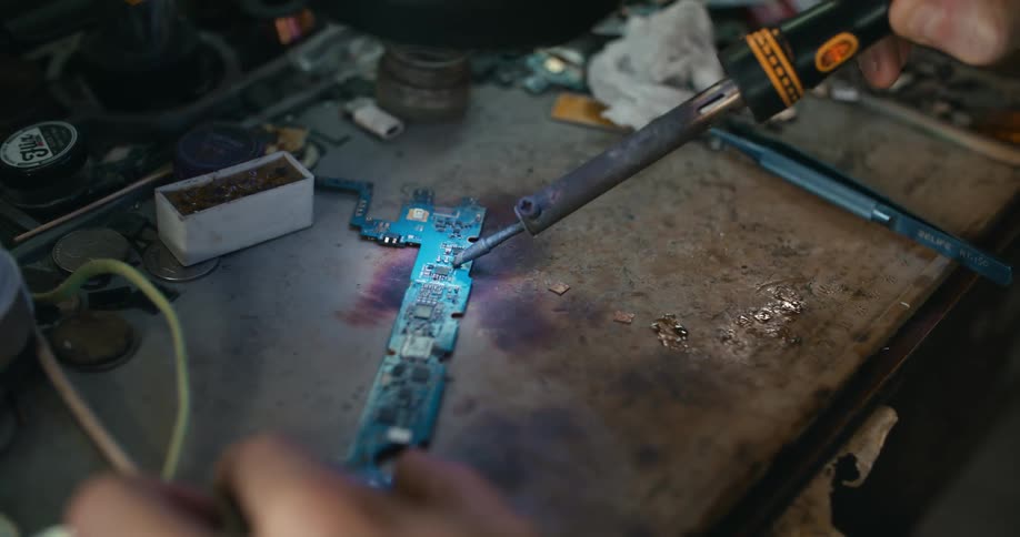 Someone is sitting at a table soldering an electronic component as they hold it steady with their left hand