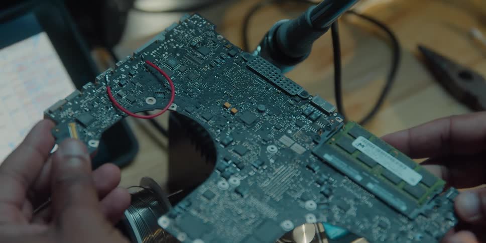 A man is holding an electronic component in his hands and he disconnects it from a machine with numbers
