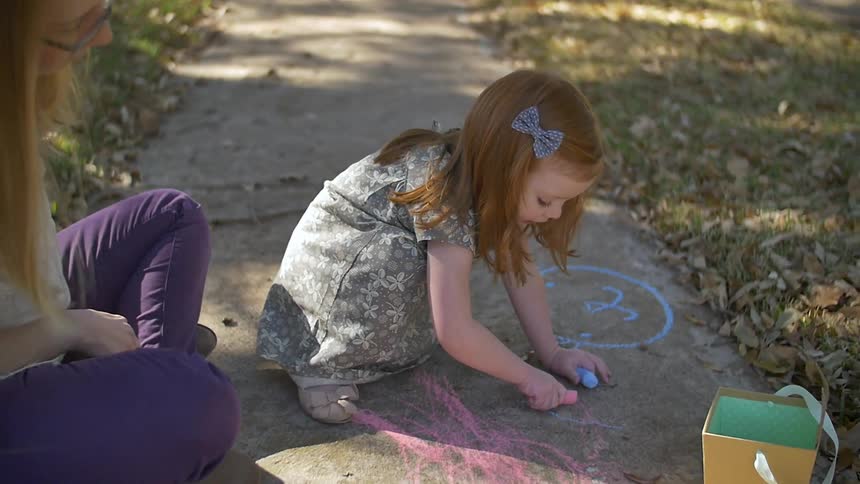 A girl and her mother draw on the sidewalk in chalk