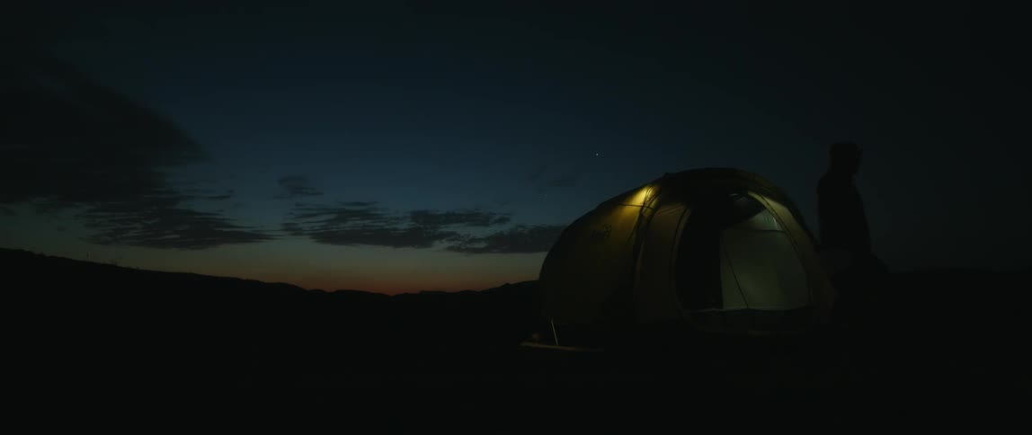 A man wearing a head lamp gathers plastic jugs then walks out of and away from his tent