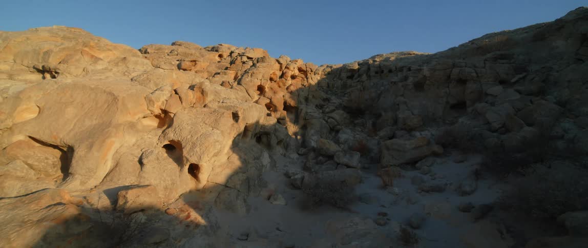 The sun shines on a rocky mountain as a shadow covers the other side and the ground below under a clear blue sky