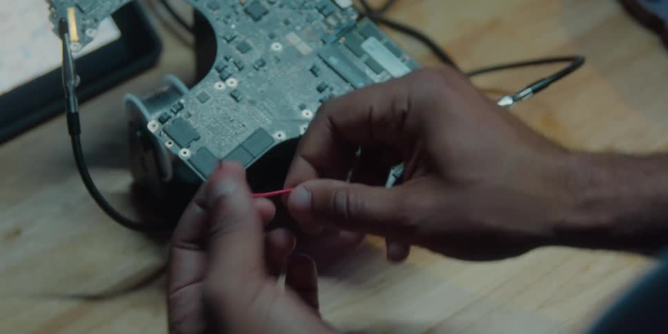 A man twists a wire as he works on a circuit board