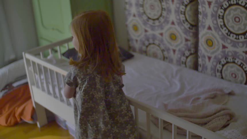 A girl walks past a small bed then turns