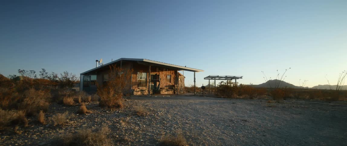 A rustic shack and pergola sit isolated in a field
