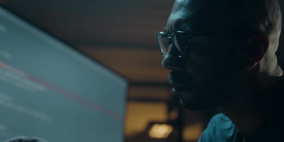A man sits in a dark office and looks at his computer