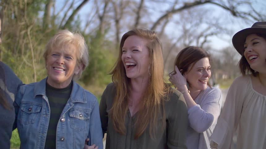 A group of women laughing and smiling as they walk along a road
