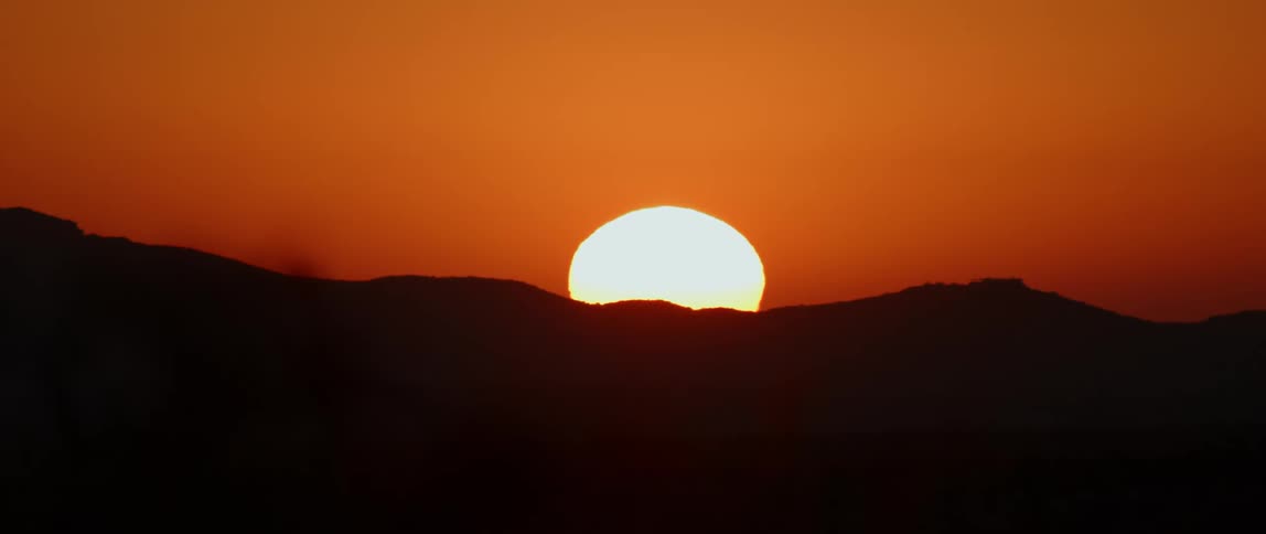 A bright sun rises over mountains in a deep red sky