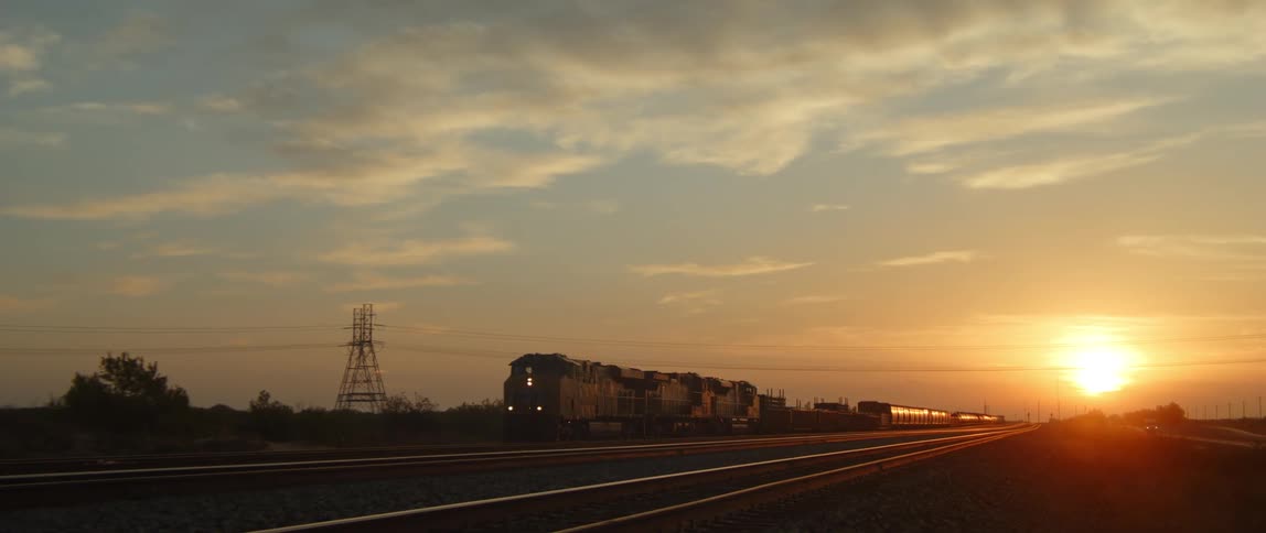 Train slowly moves along the track and away from the sun sitting just over the horizon