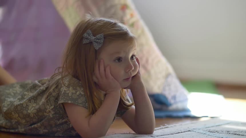 A little girl lying on the floor with her face in her hands