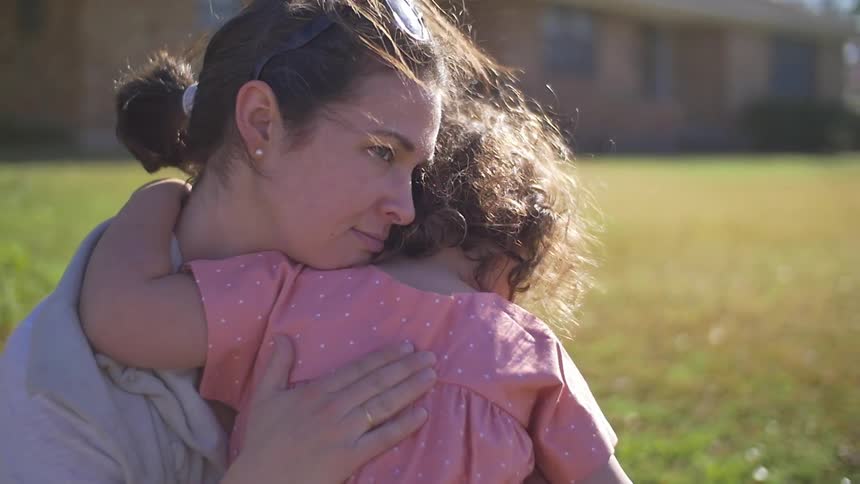 A woman hugs a girl in a yard