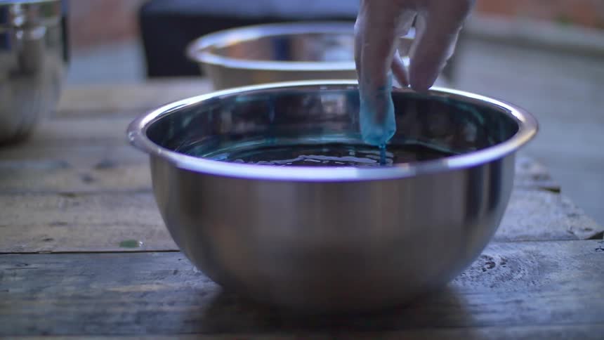 A woman stirring a bowl of liquid dye with her fingers