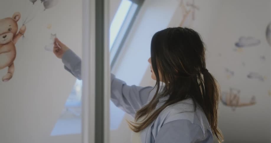 Woman with brown hair and blue shirt stick decorations to wall in room