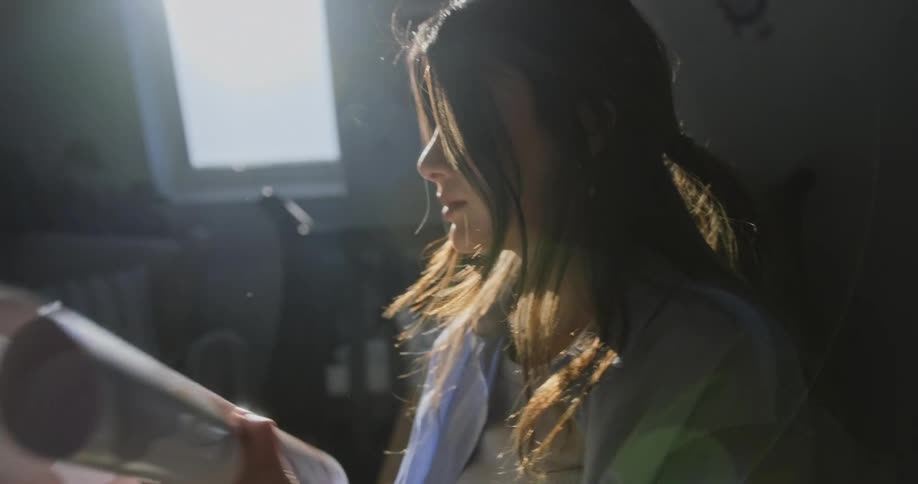 A woman is standing in a room unrolling a picture as sunlight shines in from the window