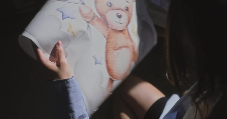 A girl is looking at a poster with a teddy bear and balloons on it