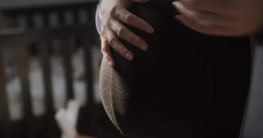 A pregnant woman is standing in a room with a smile on her face as she holds her belly