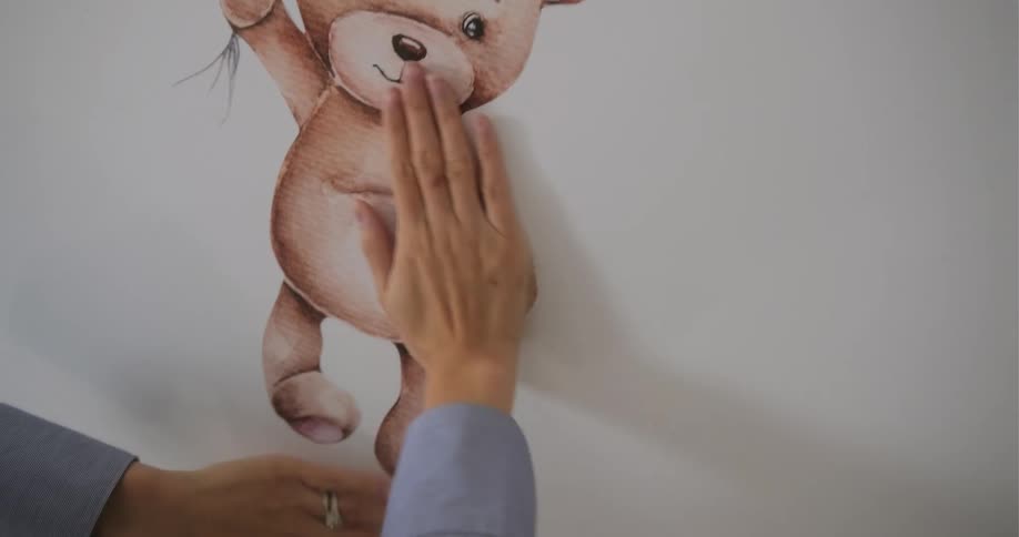 A woman applies a decal of a bear holding balloons on a wall at home