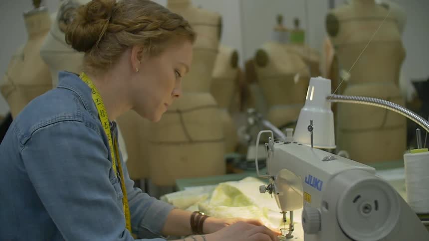 A woman sits at a sewing machine sewing fabric