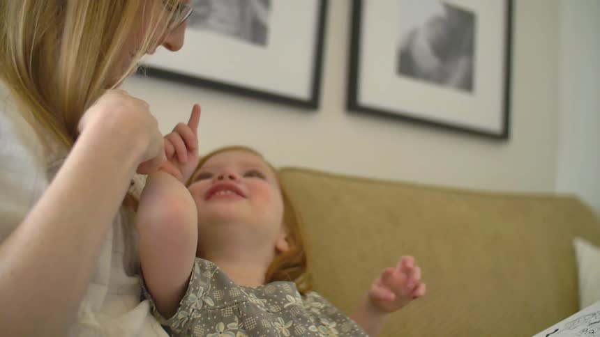 A girl in a woman's lap turns around and points at her smiling