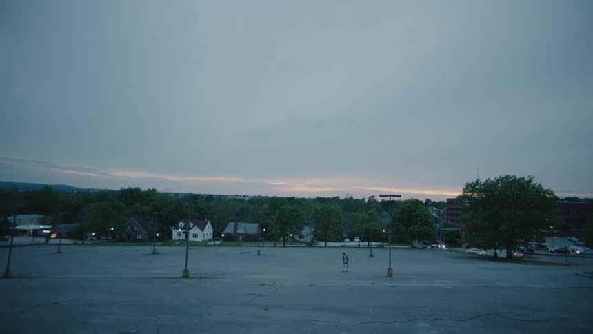 Teenager riding a skateboard on an empty parking lot on a small town at evening