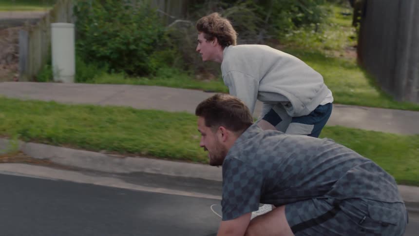 Two men skateboarding and coasting on a neighborhood street side by side