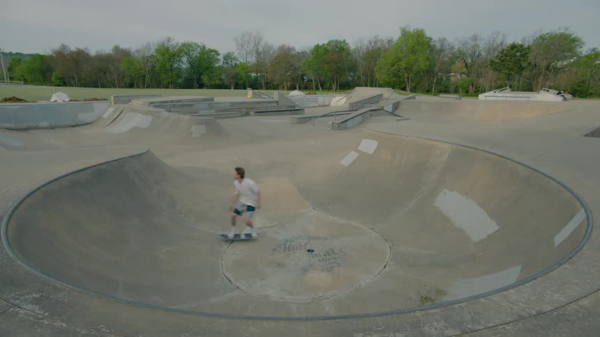 A teenage boy is riding his skateboard through a concrete bowl in a skateboard park and he leaps out into the air