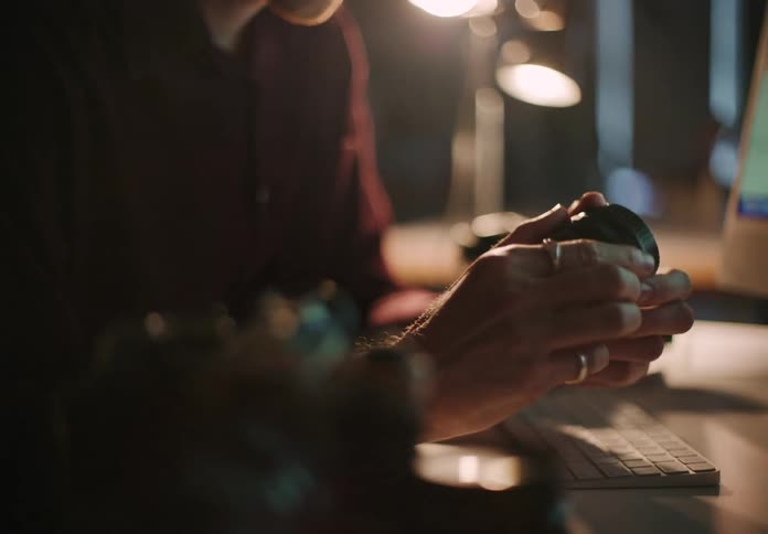 A man sits at a desk in front of a computer as he looks at a camera lens