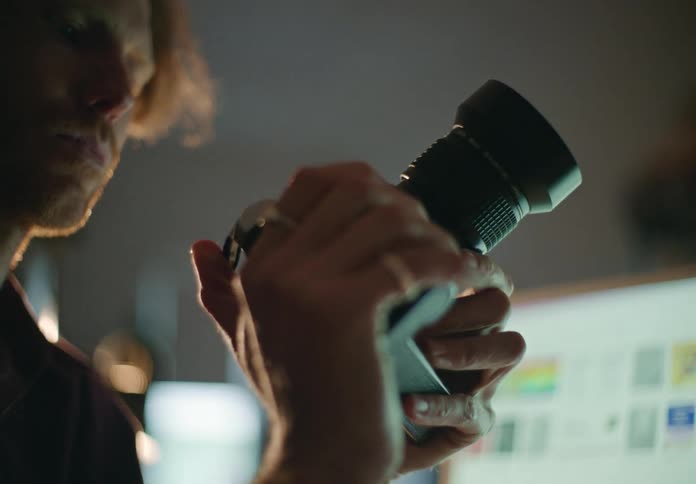 Blonde male photographer with beard uses camera next to desktop in room