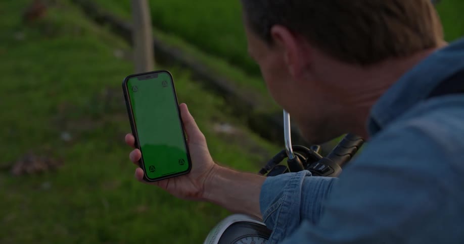 Man sitting on motorcycle leans forward to study smartphone screen