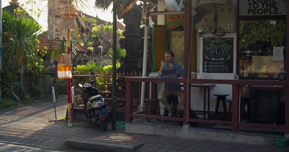 Man working on a laptop while sitting on a restaurant next to a street at evening