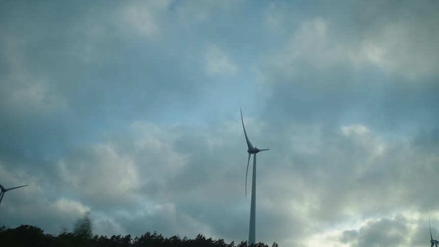 Clouds hover in the sky above a handful of wind turbines that slowly spin