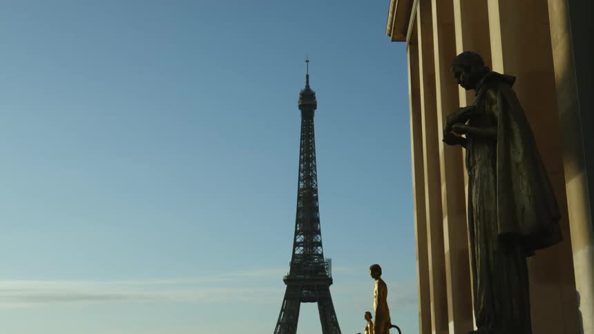 A bird flies by statues standing outside of a building near the eiffel tower in paris