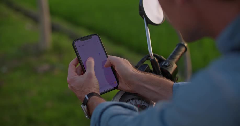 A man is sitting on a motorcycle using his cell phone with both hands