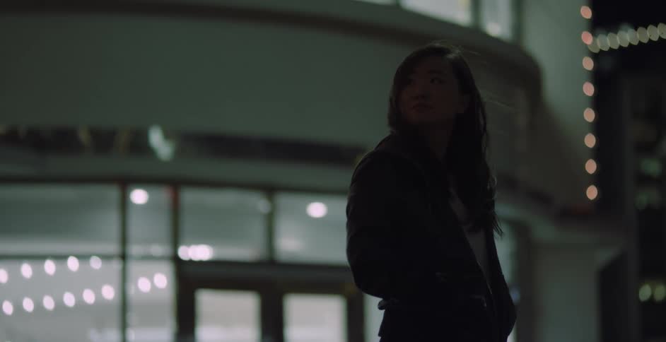 Young woman standing waiting on the outside of a building at night