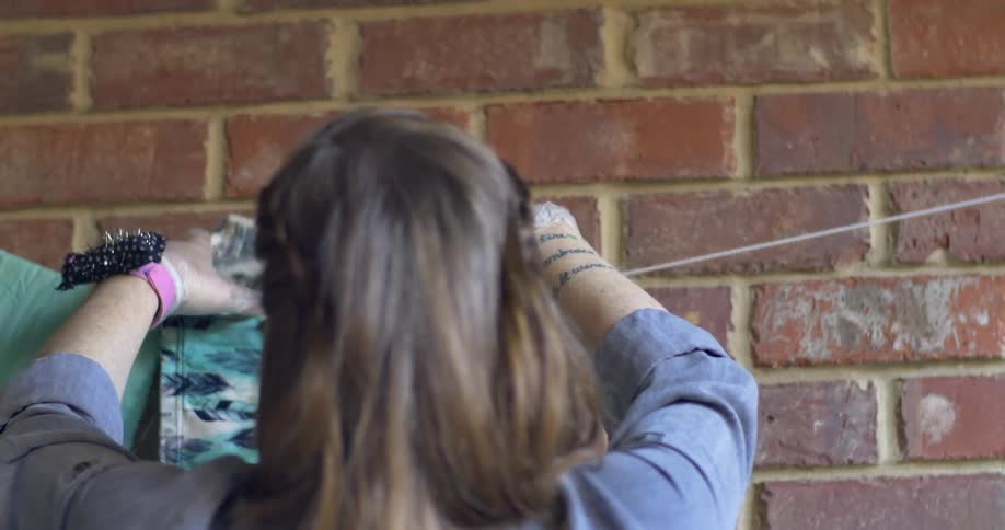 A woman hangs fabric on a line by a brick wall
