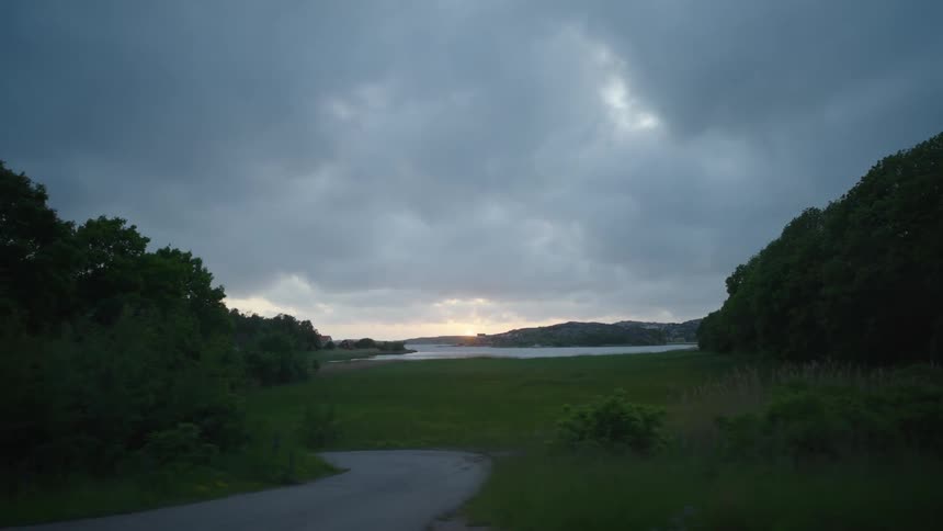 Sun setting over a calm river next to a clearing in the forest on a rural area