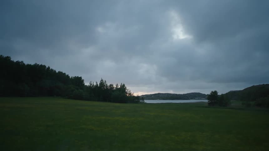 Sun setting over a calm river next to a clearing in the forest on a rural area