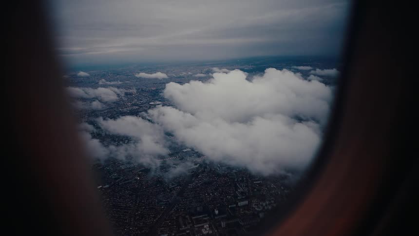 Looking out of an airplane window the neighborhoods and land below are seen through the clouds