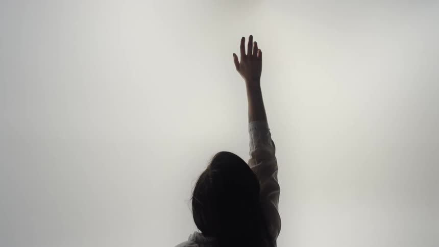 Woman with straight hair and white shirt raises her hand against the cloudy sky
