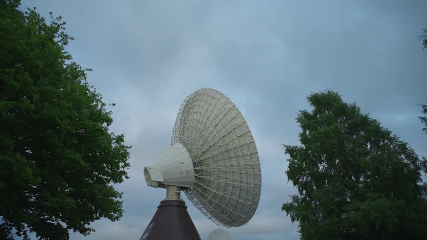 White parabolic dish surrounded by trees pointing at the blue sky
